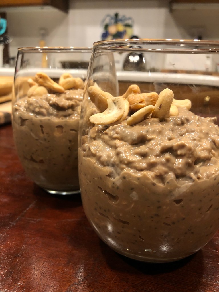 Two cups of overnight oats made with chocolate almond milk and cashew butter, topped with cashews