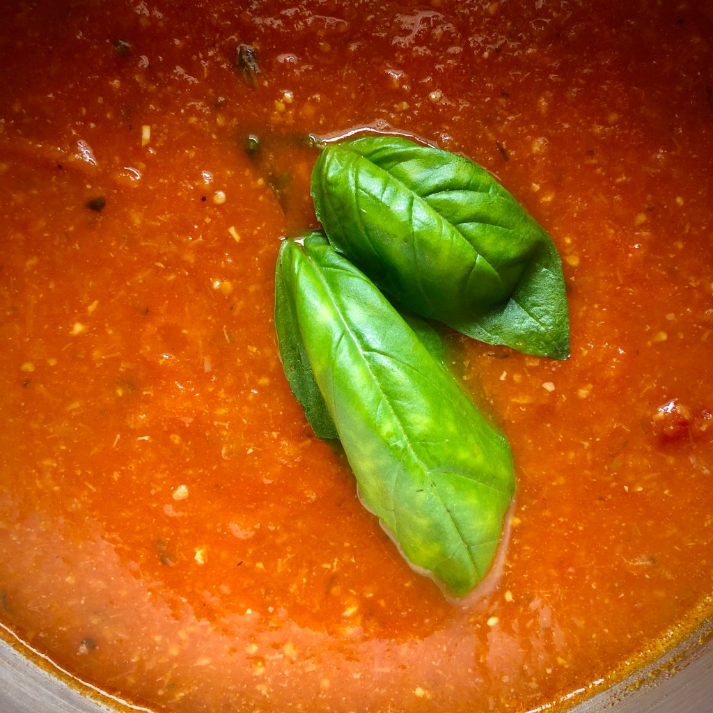Basil-Bacon Tomato Soup in a stockpot, topped with two fresh basil leaves