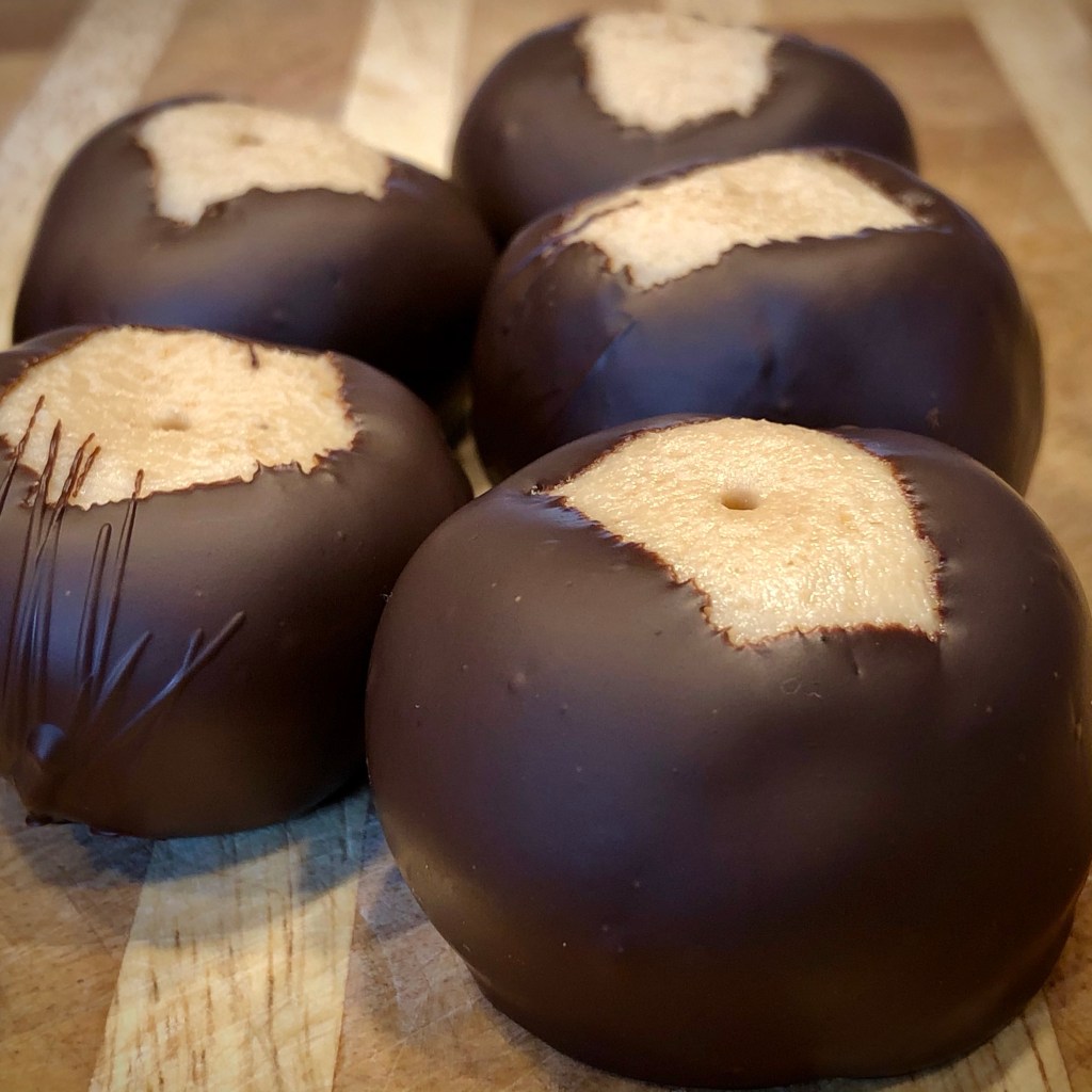 Five cashew butter buckeyes—light tan-colored fudgy candy dipped in dark chocolate   The tops are exposed, revealing the cashew butter candy underneath   